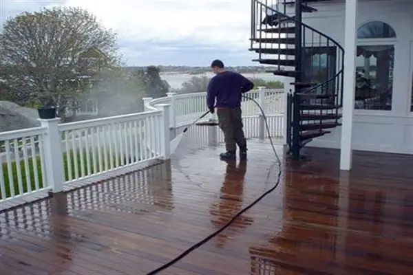 Man power washing a wooden deck with a spiral staircase and water view.